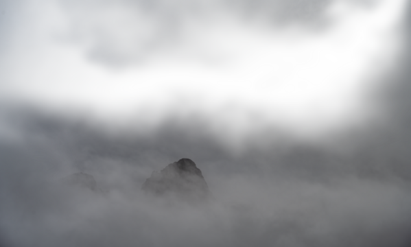 A rocky mountain peak jutting out of the mist and clouds with transparent areas
