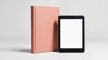 E-reader with blank screen next to coral hardcover book on white background