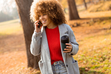 Enjoying a sunny autumn day while chatting on the phone and sipping a warm drink in the park