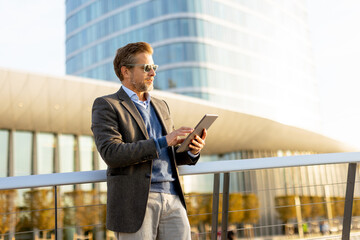 Professional man using tablet outdoors in a modern urban setting during golden hour light