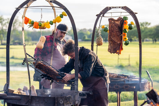 Chefs cooking BBQ and vegetables over open fire in an outdoors setting