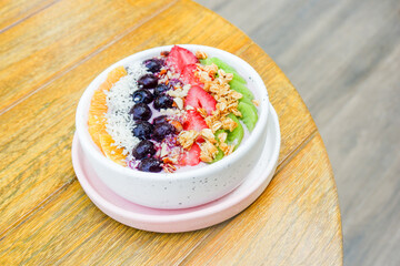 Acai bowl with strawberries, blueberries,orange,kiwi fruit,granola ,chia seeds and coconut flakes on wooden background,close-up, top view, space for text.