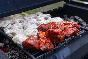 Close-up of seasoned meat grilling on a hot charcoal grill, with a mix of marinated and raw pieces.