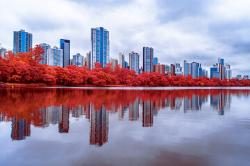 Infrared Aerochrome Photography of a Modern Urban Skyline Reflecting in a Calm Lake Surrounded by...