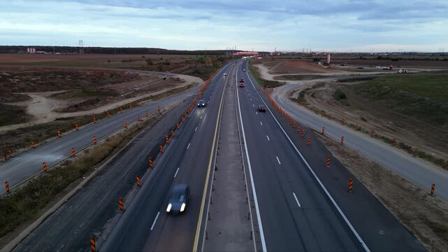 Low-altitude drone view from a newly paved highway overpass overlooking an active motorway during road construction. Modern transportation infrastructure with moving traffic, construction works and ex