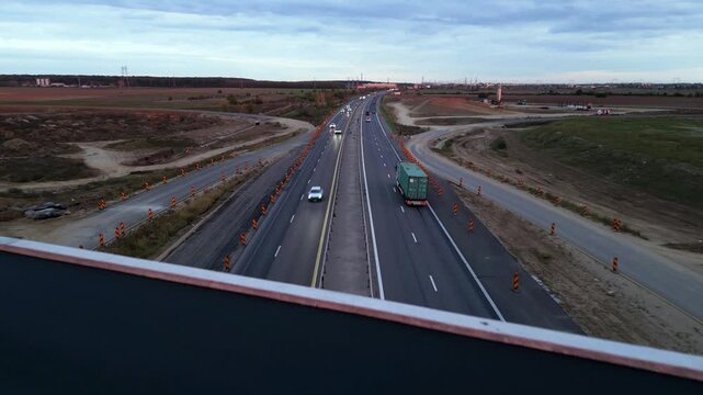 Low-altitude drone view from a newly paved highway overpass overlooking an active motorway during road construction. Modern transportation infrastructure with moving traffic, construction works and ex