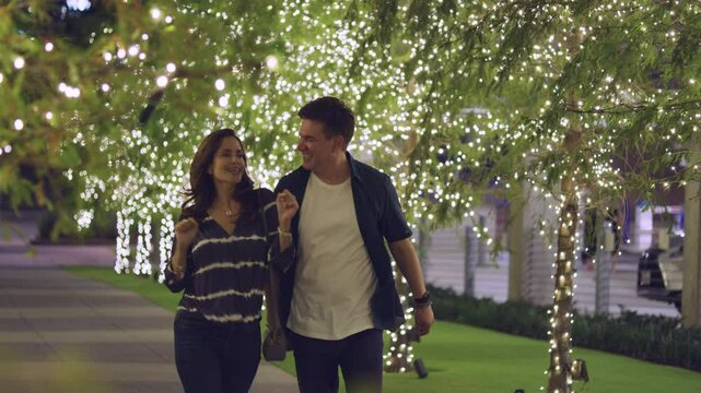 Two people playfully chat and dance as they walk through a tree lined walkway