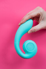 Hand with blue vibrator sticking out through pink paper background. Vertical photo. 