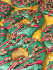 Um conjunto de donuts decorados com cobertura verde e gotas de chocolate no topo. Em exposição para venda.