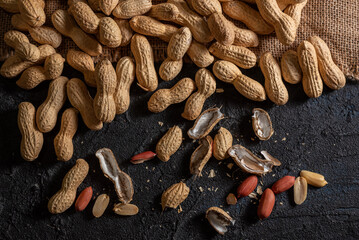 Plano cercano de cacahuetes con cáscara esparcidos sobre una superficie oscura.