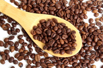 On a white background lies a wooden spoon with coffee beans.