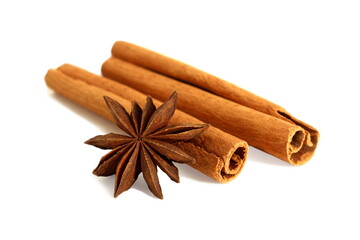 On a white background lie the cinnamon spice, two sticks and an anise flower.