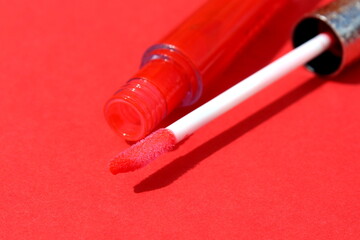 There is a red lip gloss with a brush on a red background.