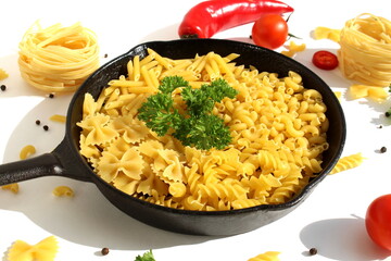 A cast iron frying pan with dry pasta and fresh vegetables stands on a white background.	