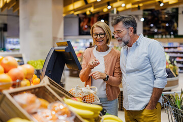 Senior couple weighing fresh fruit at supermarket self service scale