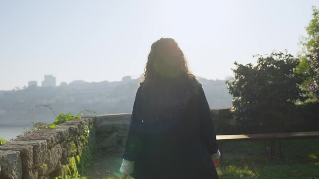 Young woman walking with raincoat in a park overlooking Douro River in Porto. Beautiful sunlight as female tourist or student enjoying quiet and peaceful day in Parque das Virtudes at sunset
