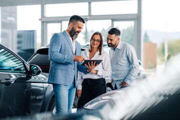 Interactive teamwork with tablet among cars in dealership.