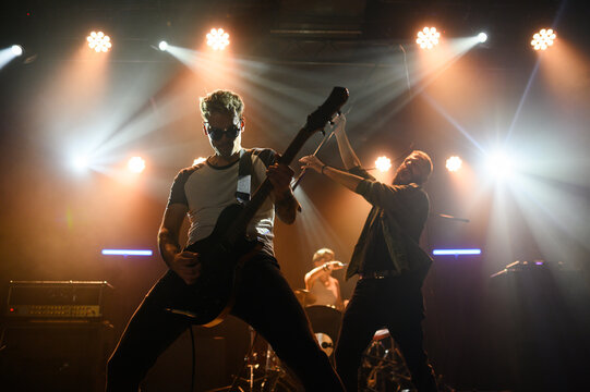 Rock band performing live on stage with energetic guitarist and violinist