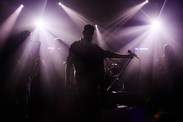 Singer performing with band on stage under purple lights