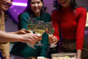 Group of friends celebrating christmas together, raising glasses of white wine for a festive toast