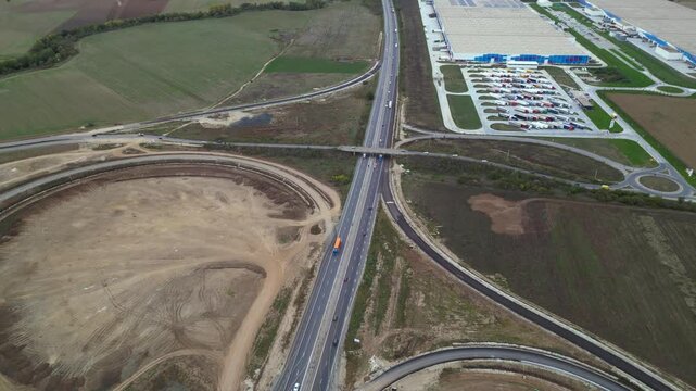 Top-down drone view of a newly built highway cloverleaf interchange with looping ramps, overpasses and active motorway traffic. Large-scale transportation infrastructure and civil engineering project 