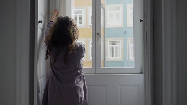 Woman standing in front of window open and close curtain blocking light. Silhouette of young shy female in her apartment or hotel or house roll open white drapes then shuts to complete darkness