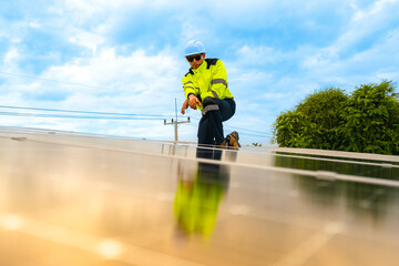 A technician in safety gear inspects solar panels on a metal rooftop, holding a tool. The scene...