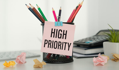 High Priority text written on sticky in hands on office background