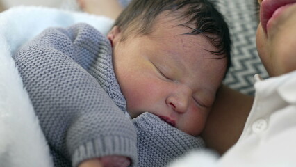 Close-up of a sleeping newborn wrapped in a cozy blanket, resting peacefully in the arms of an...