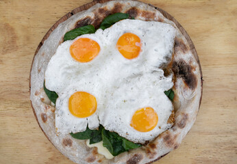 Top view of a pizza with mozzarella cheese, spinach and fried eggs, on the wooden table.
