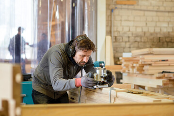 A focused craftsman uses a router in a woodworking shop, showcasing precision and skill in a professional workshop setting