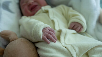 Newborn baby resting in a crib, covered in a soft, white blanket, moving slightly, showcasing the tranquility and comfort of early childhood, and the tender care given to newborns in their first days