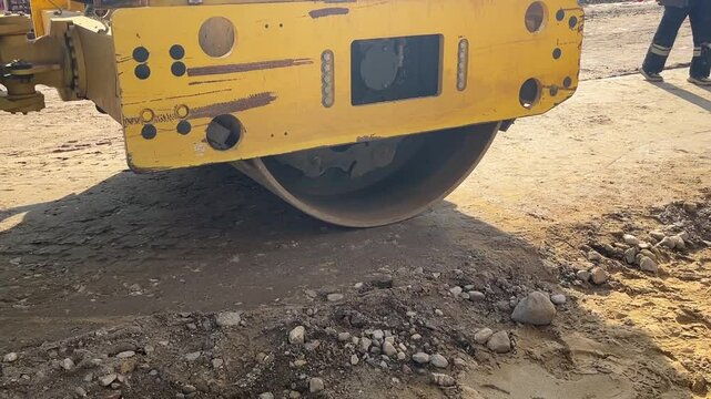 A yellow and black construction vehicle is rolling over a dirt road. The back of the vehicle is covered in mud