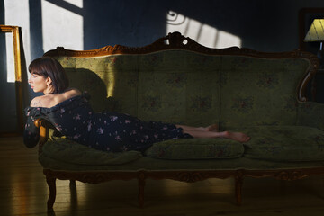 Woman in floral dress lounging on an antique green sofa