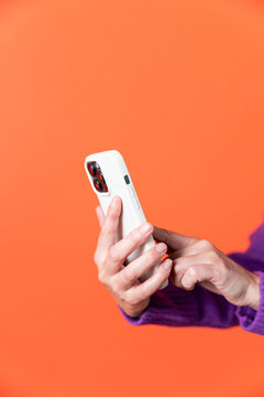 Close-up of hands using a smartphone on a vibrant orange background