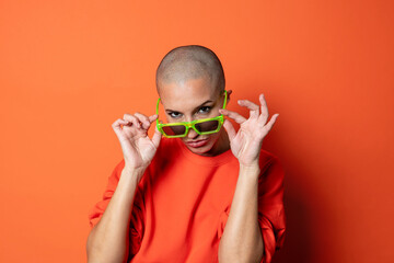 Bold bald adult woman in orange with striking green glasses