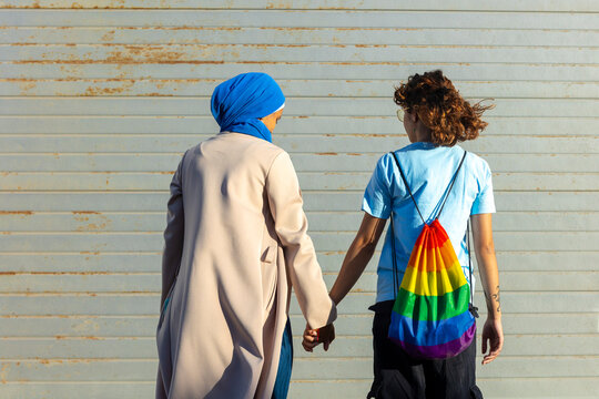 Lesbian couple with Muslim partner holding hands, showing pride