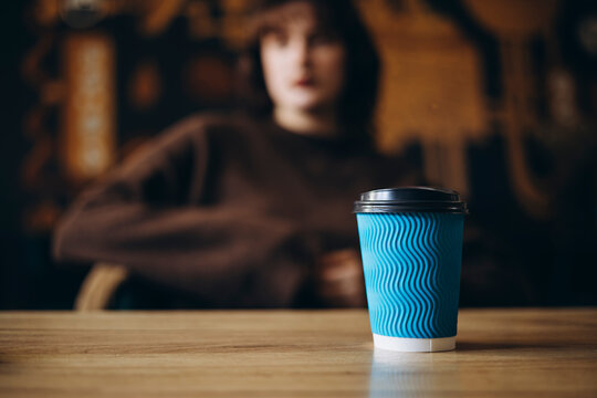 Blue coffee cup on wooden table with blurred person in background