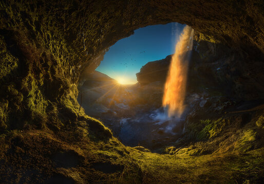 Majestic waterfall in cave during sunset with sun rays