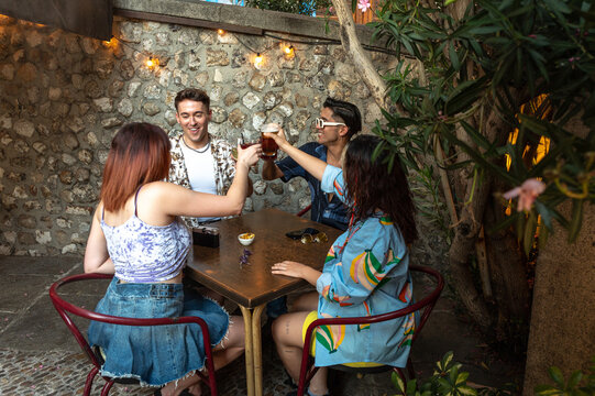 Four friends toast with beer at an outdoor table