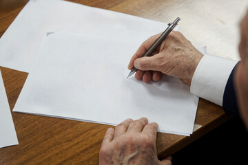 An elderly man in a business suit writes with a pen on a piece of paper. Concept of making a will...