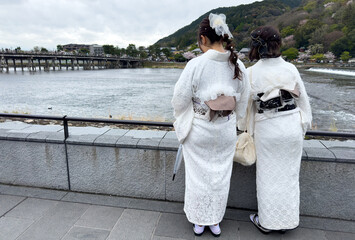 Two young women in traditional Japanese dress looking at Uji river and bridge. Kyoto, Japan.