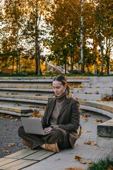 Fototapeta premium woman working remotely in a beautiful autumn park, sitting on a bench with a laptop. The serene outdoor environment is perfect for remote work or study, surrounded by fall foliage.