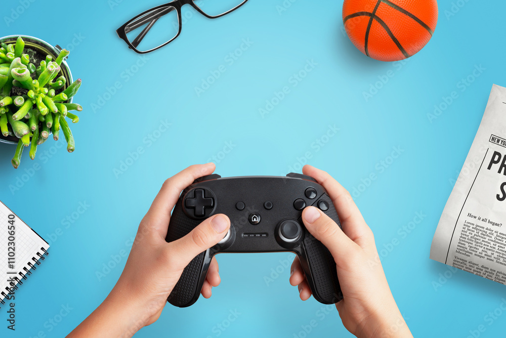 Poster top view flat lay composition of a player holding a gamepad on a desk with a ball, newspaper, glasse