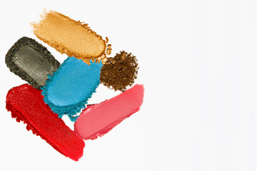 Cosmetic texture composition with vibrant lipstick, eyeshadow, bronzer, glitter, and powder with empty space on a light white background.