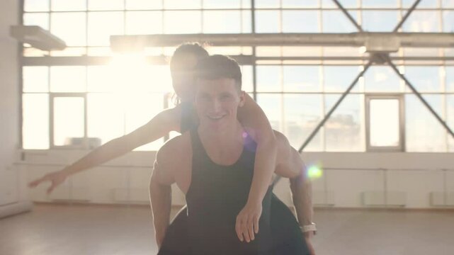 Athletic happy couple in sportswear runs in sunlight in a sports gym, the guy carries the girl on his back and smiles, the concept of freedom, 4K UHD B-Roll footage