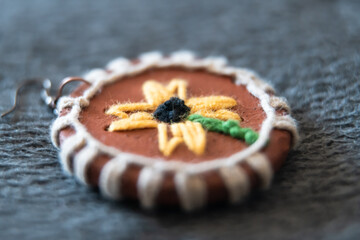 A handmade terracotta ornament featuring a sunflower design, intricately woven with yarn, creating a unique blend of natural materials and textile art