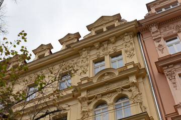 There is a large building that showcases numerous windows, and situated right in front of it is a beautiful tree providing shade