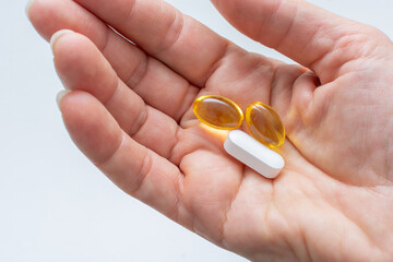 Close up of female open palm with yellow Omega-3 fatty acid capsules and magnesium tablets on light...