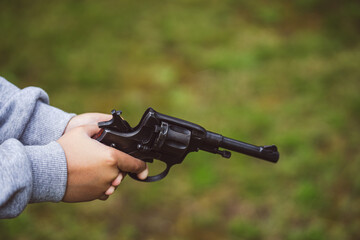 Revolver of the Nagant system with a black body and a long barrel.The gun is in the hands of a teenager.Child crime.